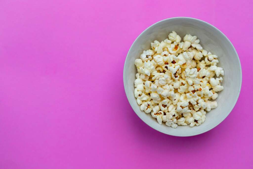 bowl of popcorn on hot pink background photo by Yulia Khlebnikova