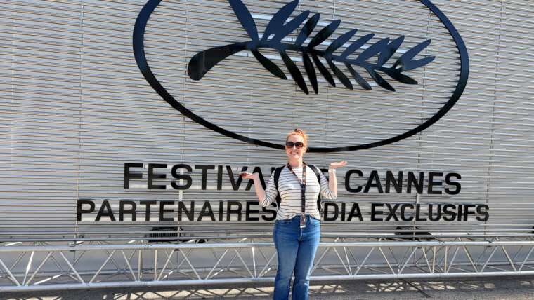 Jennifer Coté standing with her arms raised in front of the Cannes Film Festival sign in Cannes, France.